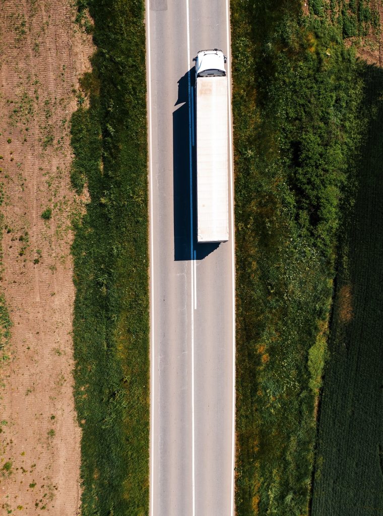 Aerial shot of semi-truck driving along the highway through countryside landscape, drone pov directly above on sunny spring day. Transportation and logistics concept.
